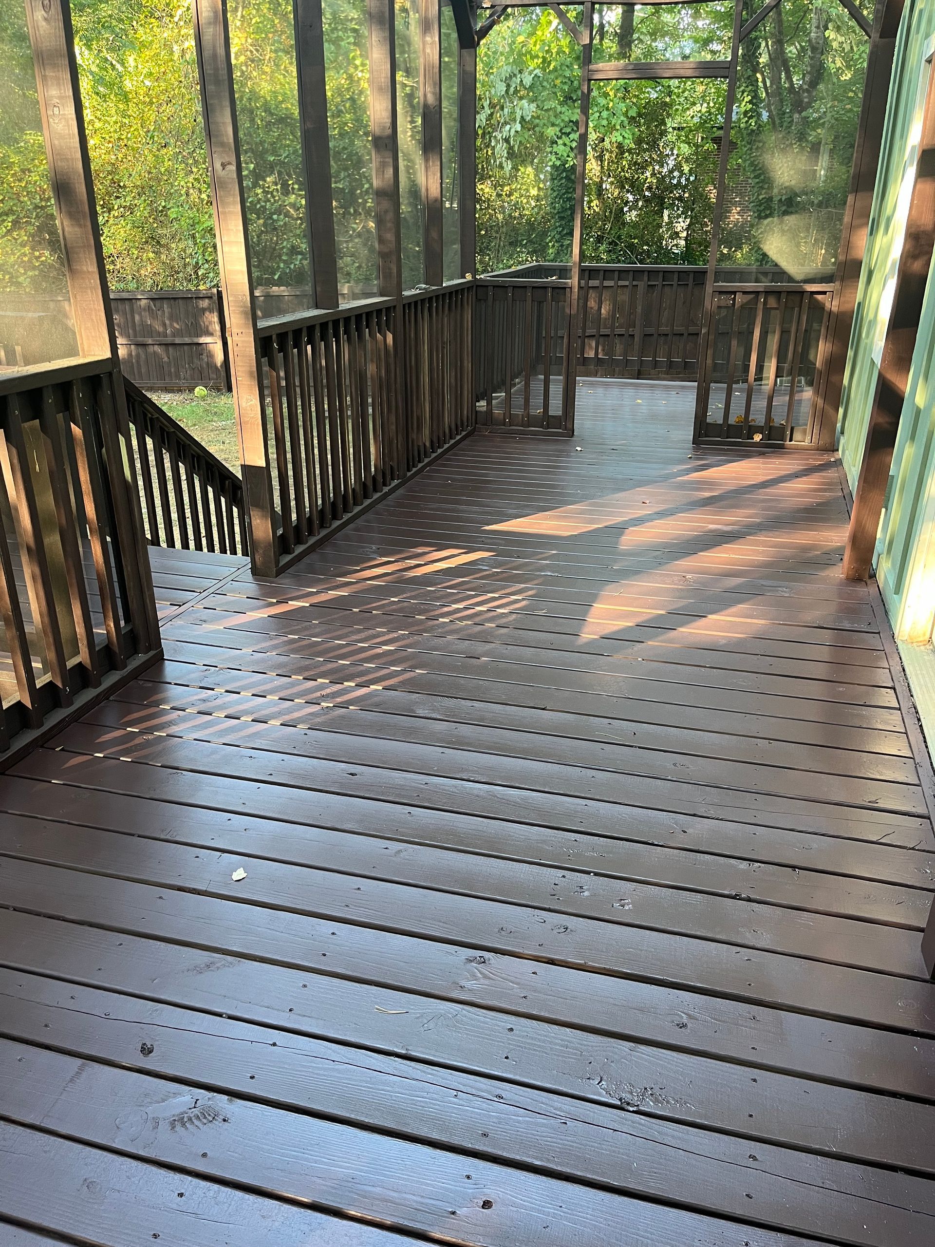 Wooden deck walkway with railings in a wooded area, dappled with sunlight.
