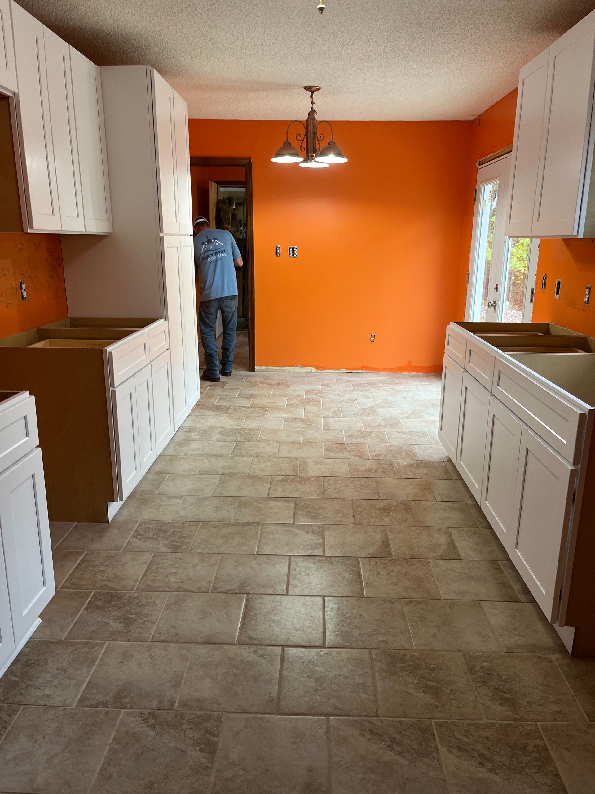 Kitchen with orange walls, white cabinets, and a person standing near the back doorway.