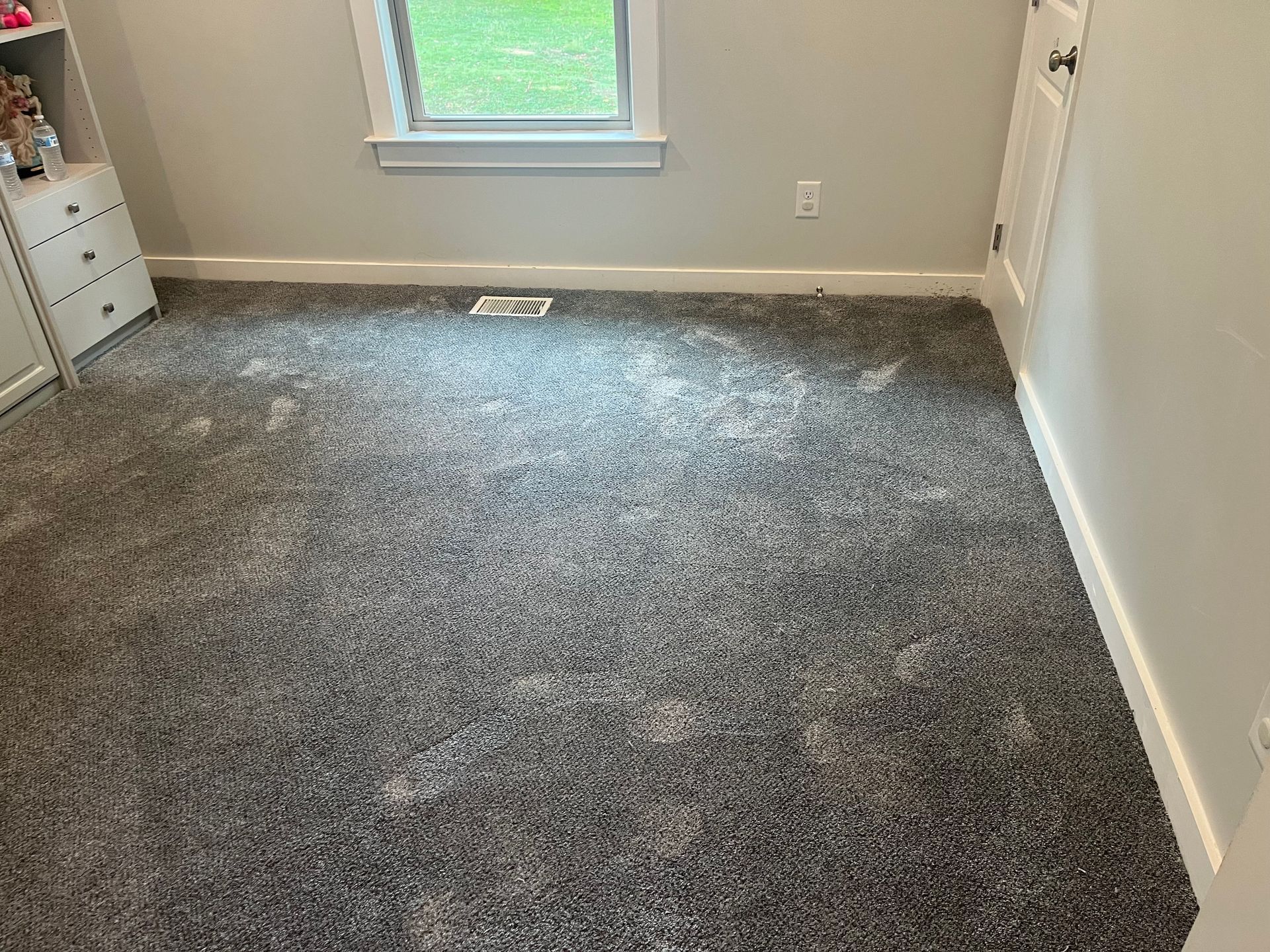 Empty carpeted bedroom with a window, beige walls, and white trim.
