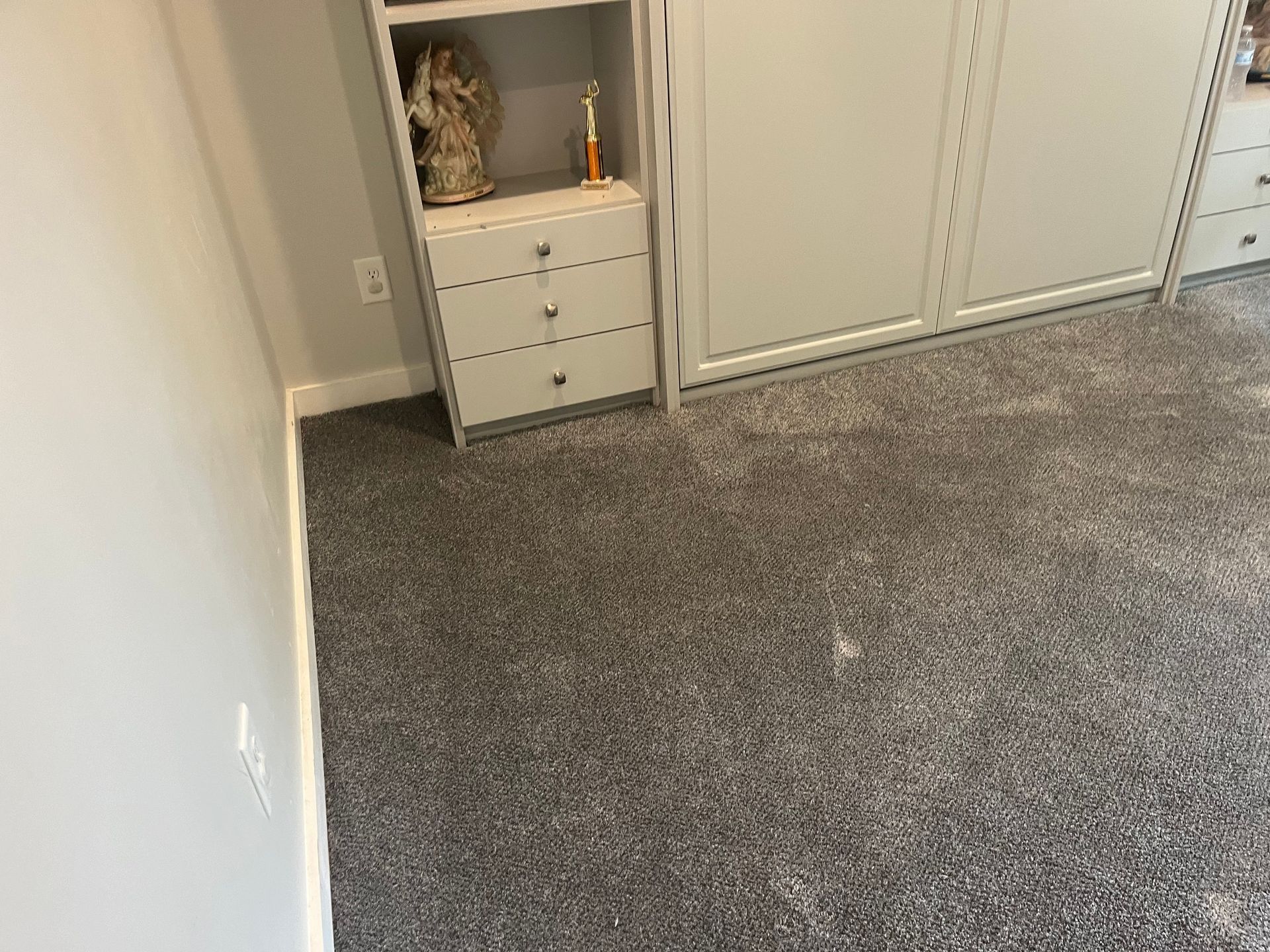 Empty carpeted bedroom corner with a small white dresser and sliding closet doors.