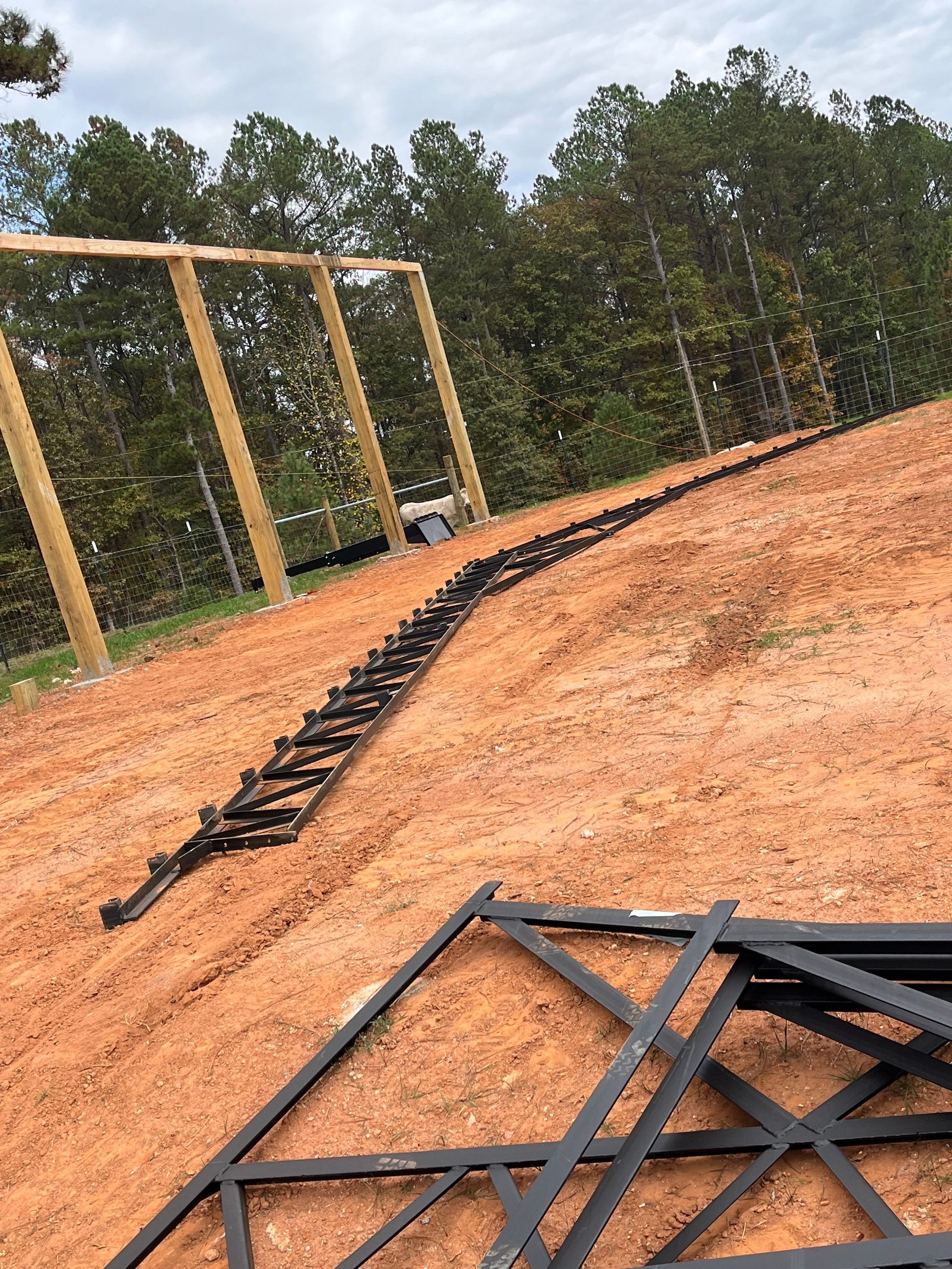Outdoor dirt lot with scattered black metal frame pieces and wooden posts under a cloudy sky
