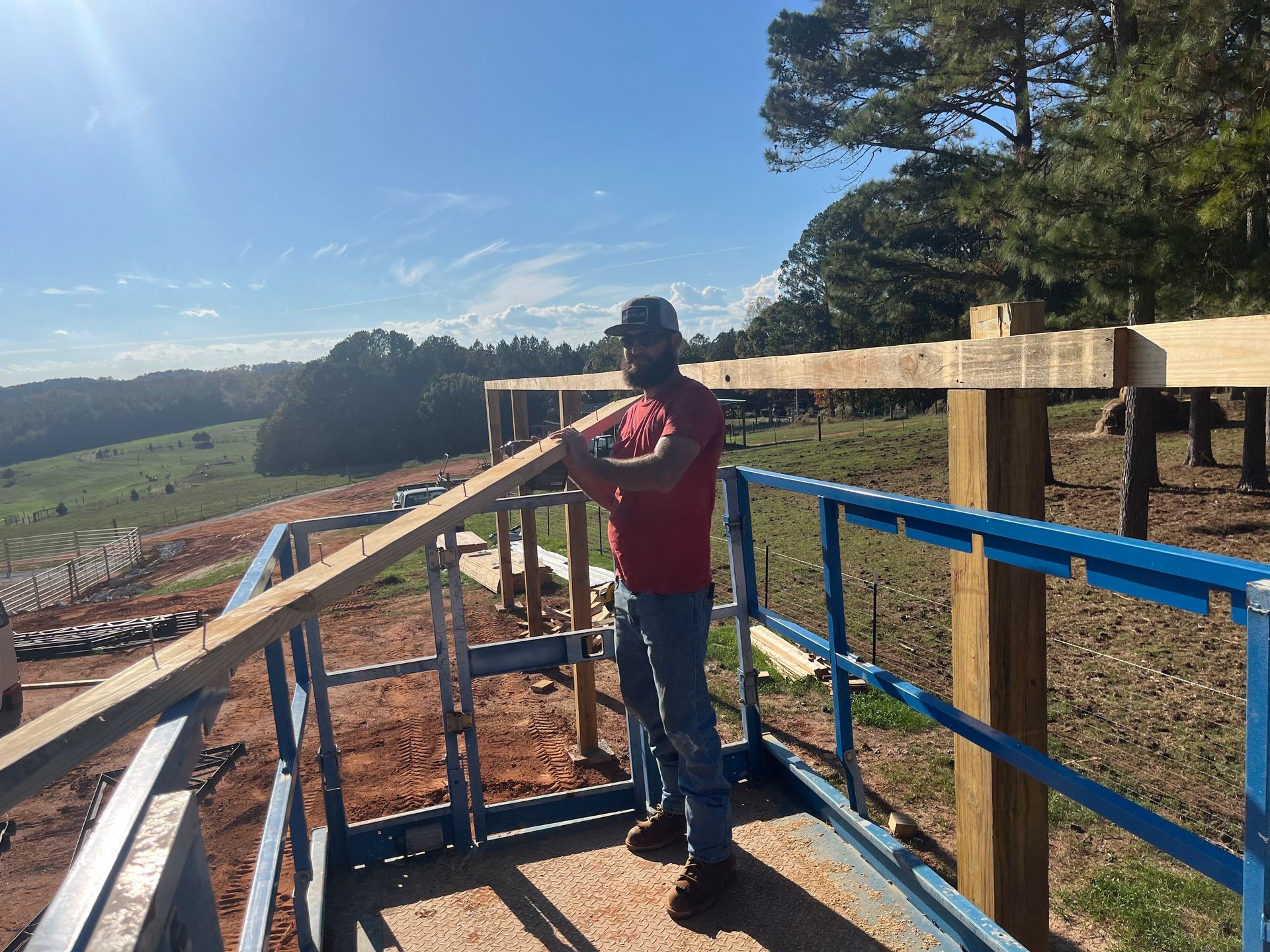 Person standing on a porch under construction, looking over a rural landscape on a sunny day