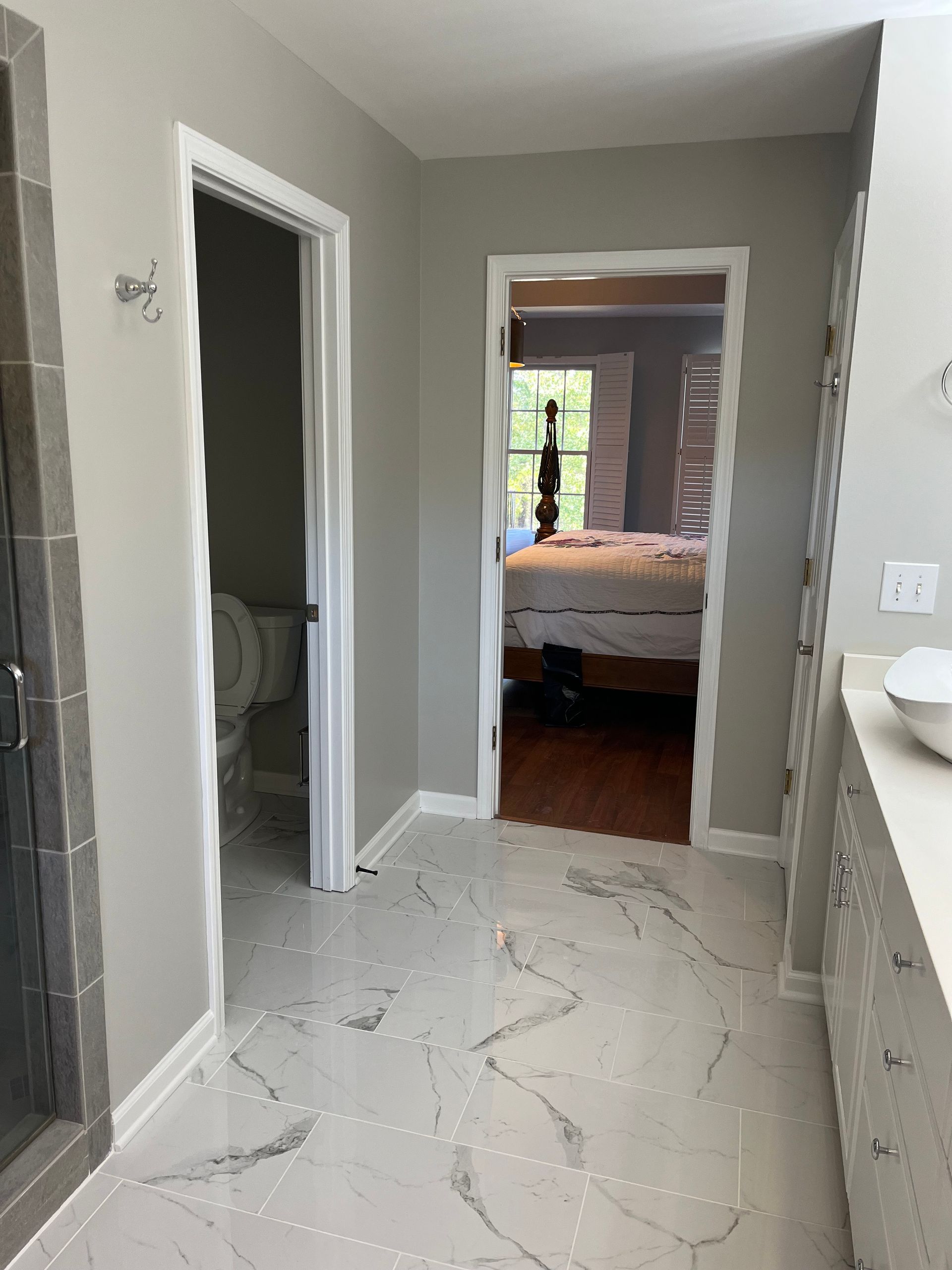 Narrow hallway with gray walls, marble-patterned floor, and open doorways leading to a bedroom.