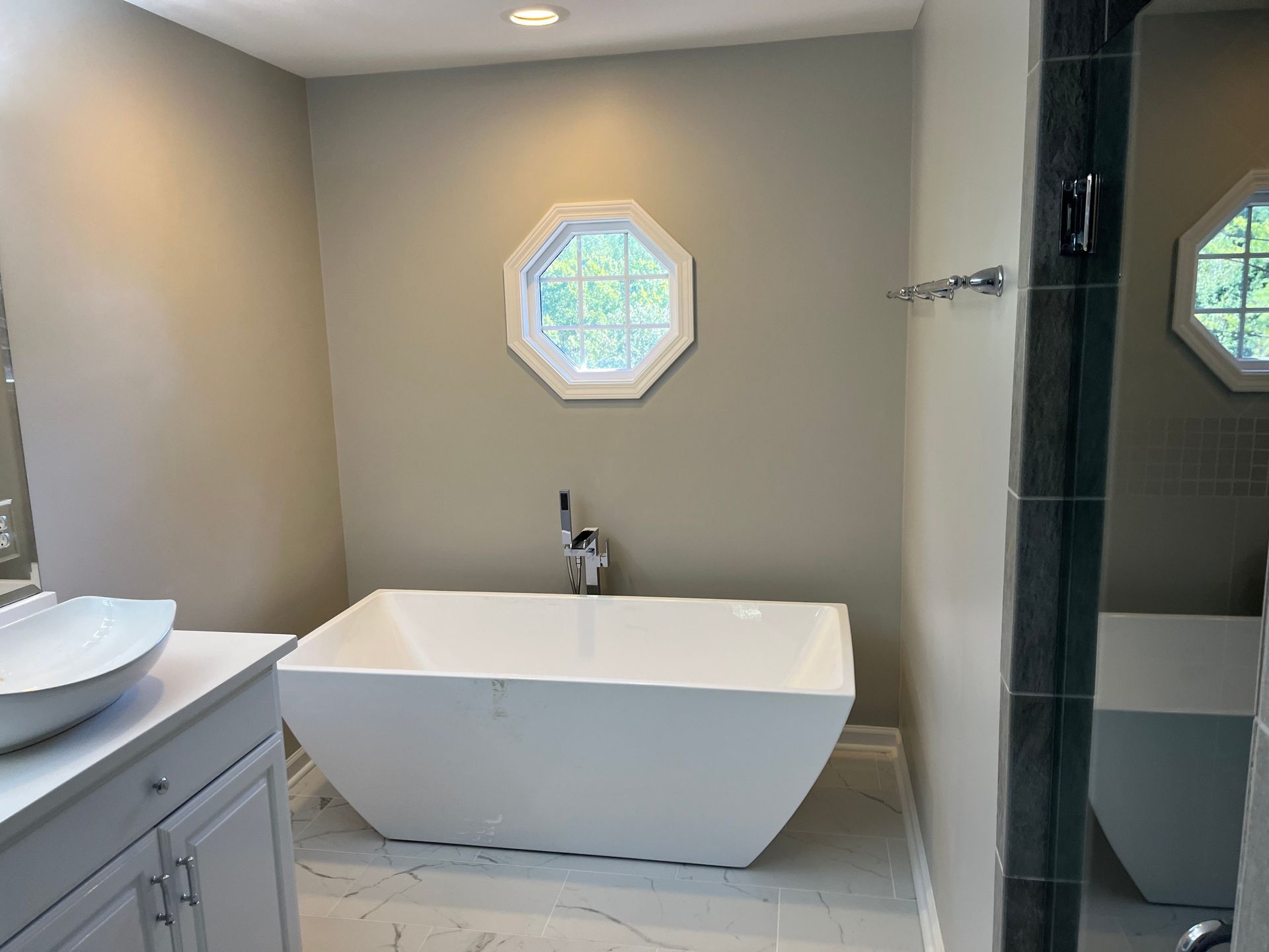 Modern bathroom with a white freestanding tub, gray walls, and octagonal windows above the tub