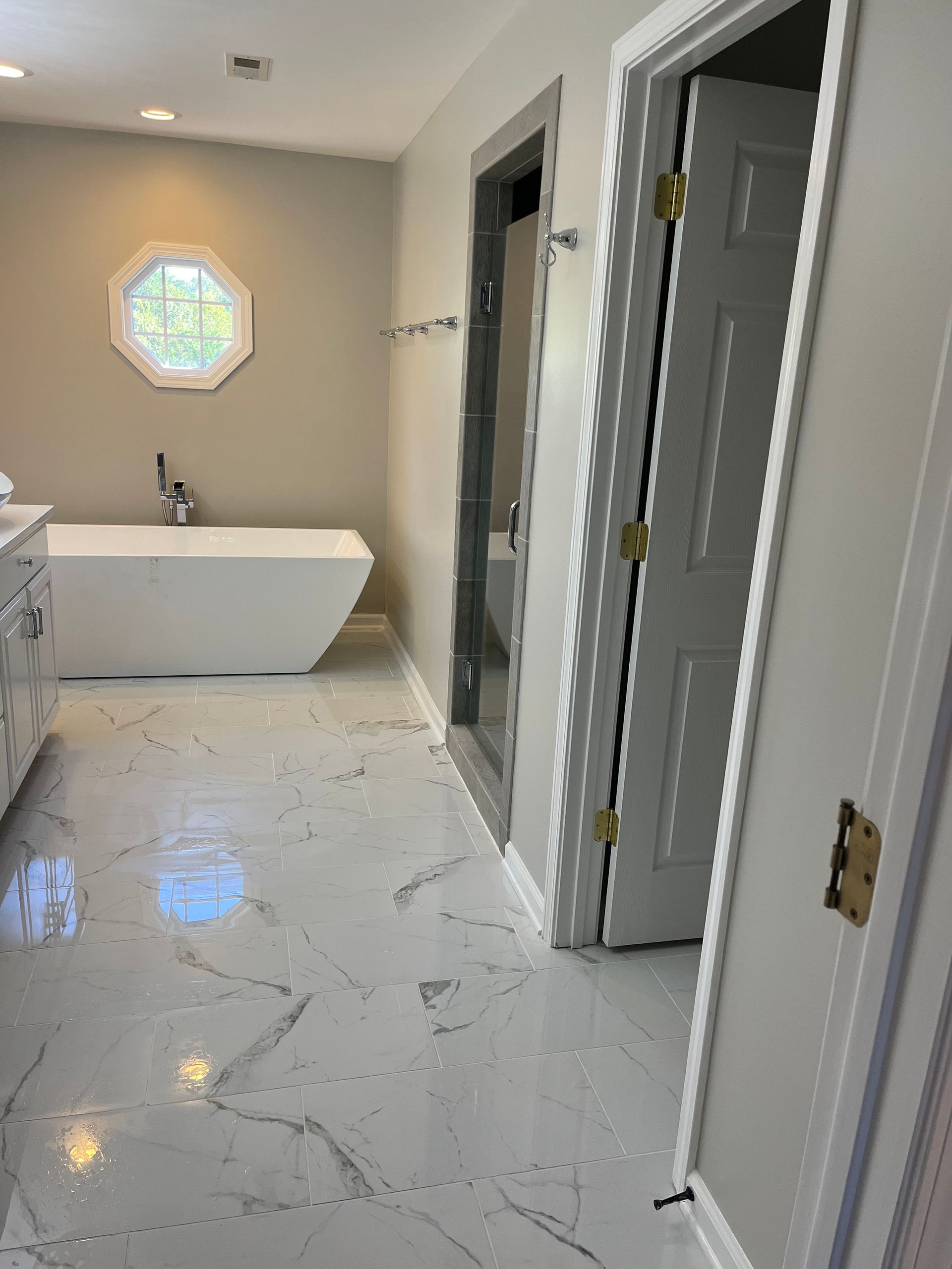 Bathroom with freestanding tub, octagonal window, and white marble tile floor under renovation.