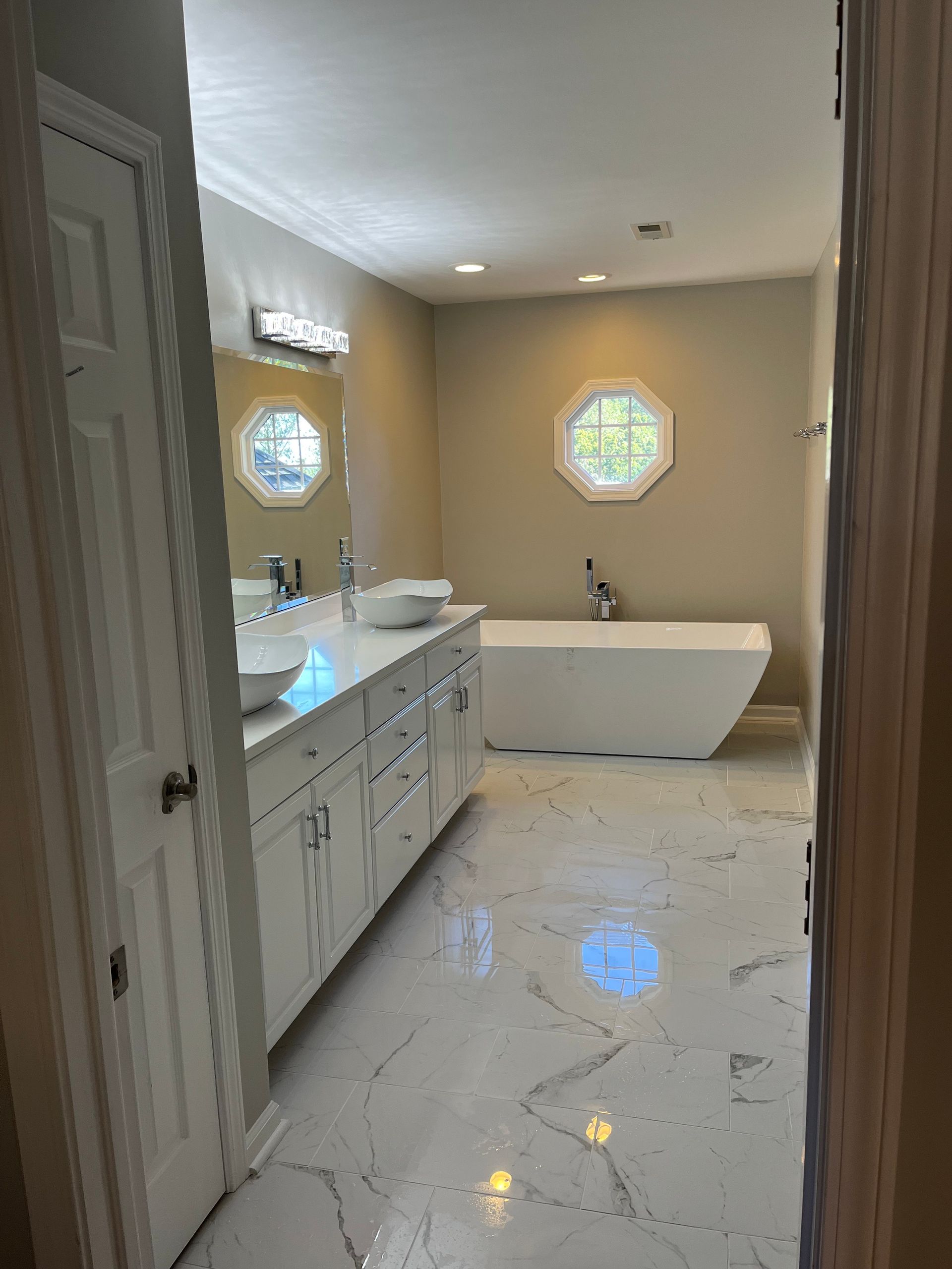Bright bathroom with double vanity, marble floor, and freestanding tub beside octagonal windows.