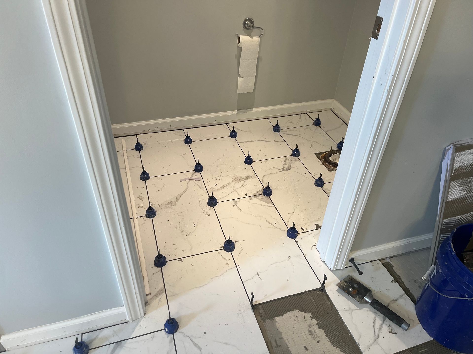 Small bathroom under renovation with white patterned tile floor and tools on the right.