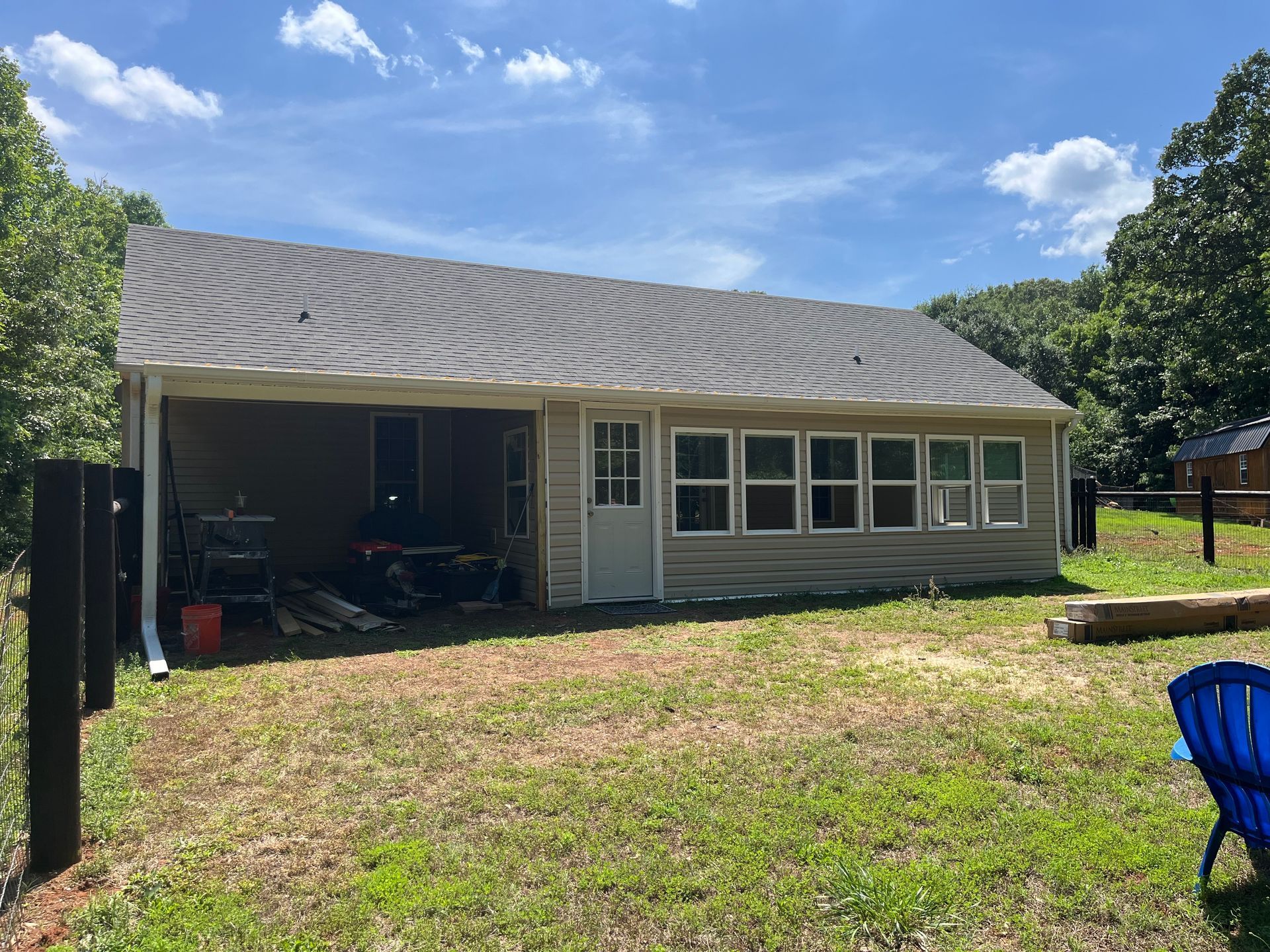 Single-story house with a covered carport, white siding, and a grassy yard under a blue sky.