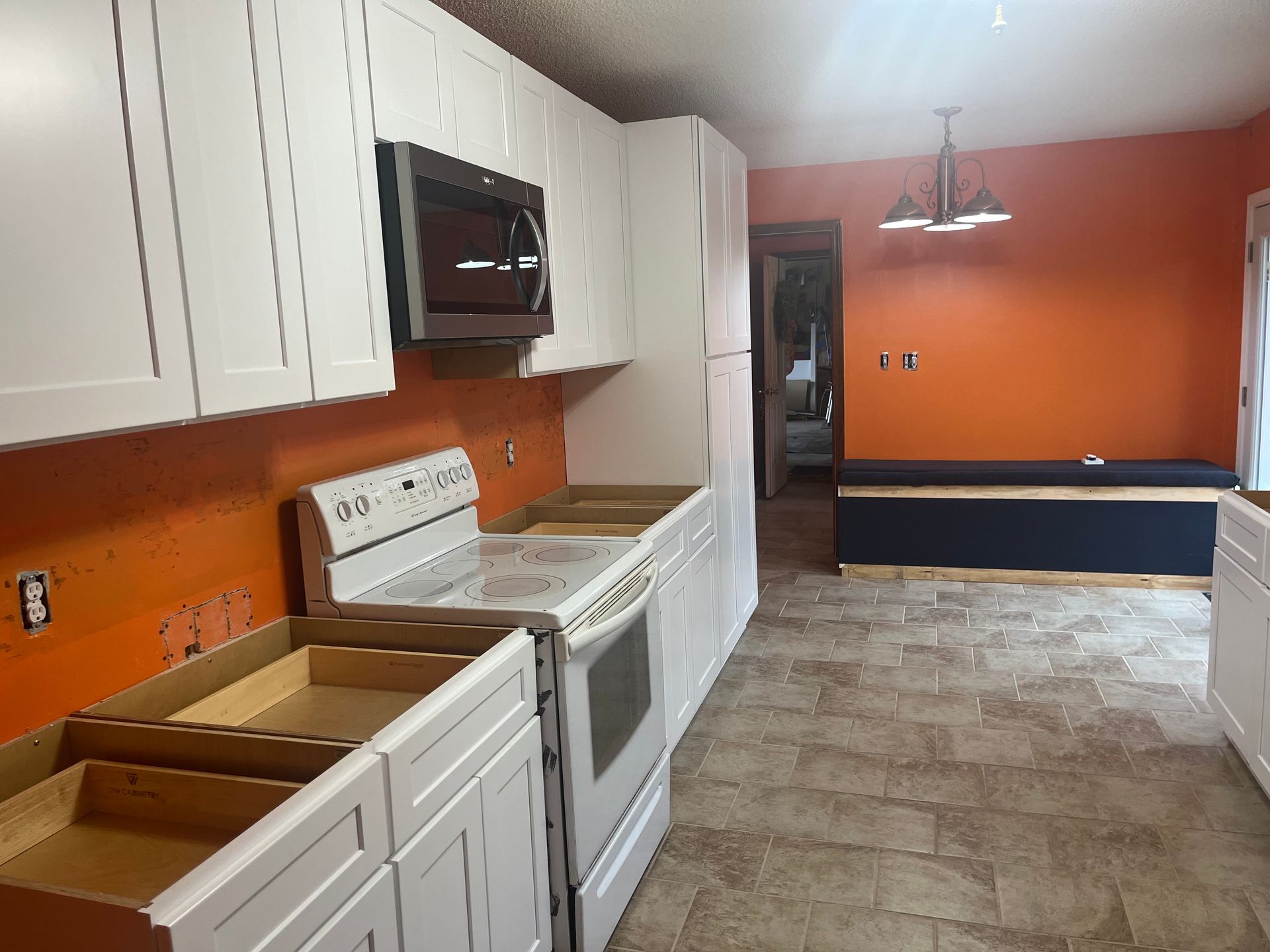Empty kitchen with white cabinets, orange walls, white stove, and tiled floor.