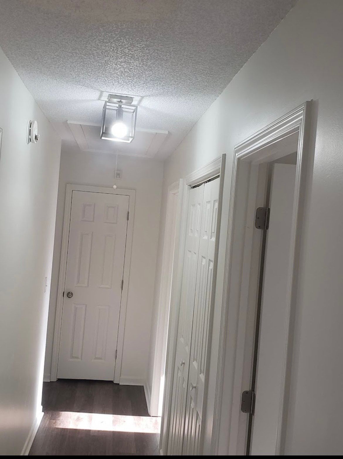 Narrow white hallway with doors, ceiling light, and sunlight on the floor