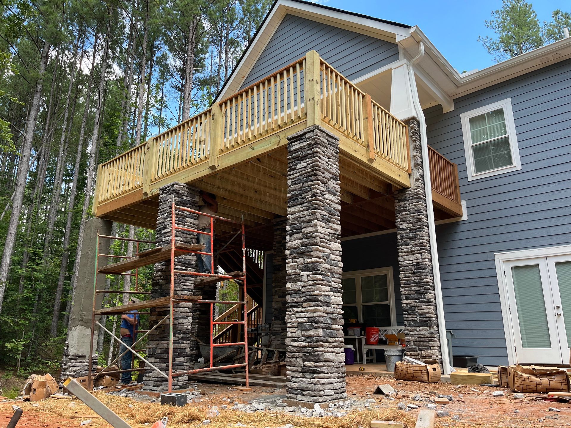 House with stone deck supports and unfinished balcony under construction in a wooded area