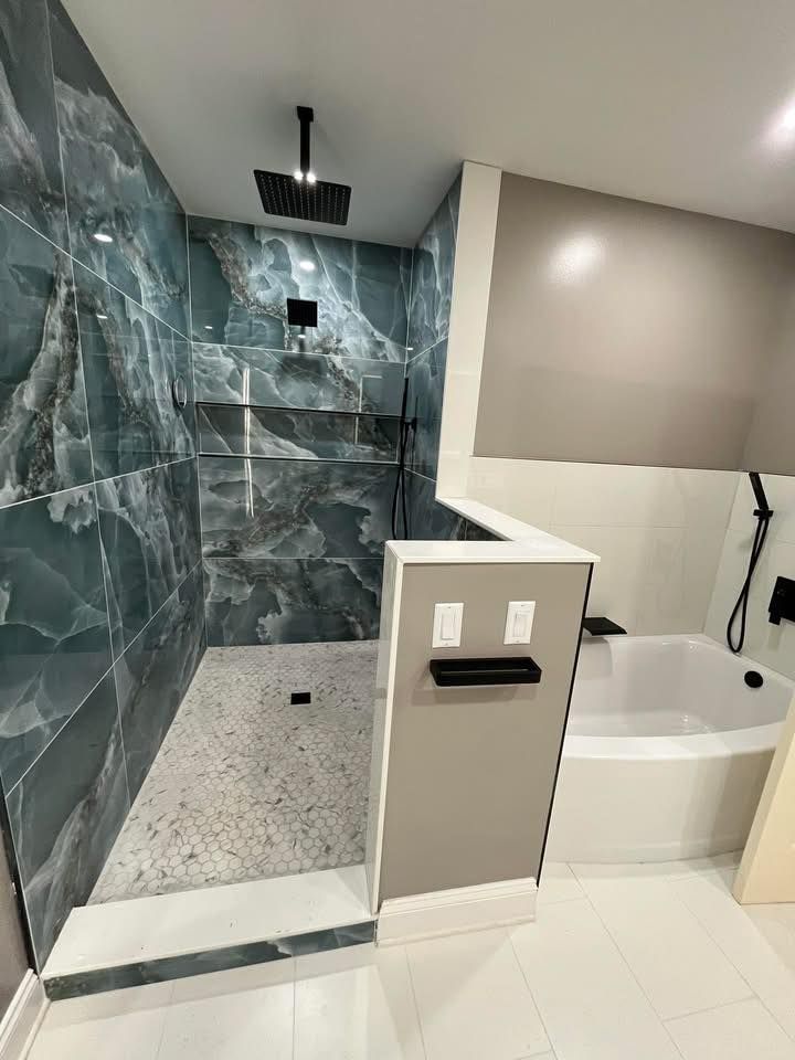 Modern shower and bathroom with blue marble tile, glass shower enclosure, and white tub.