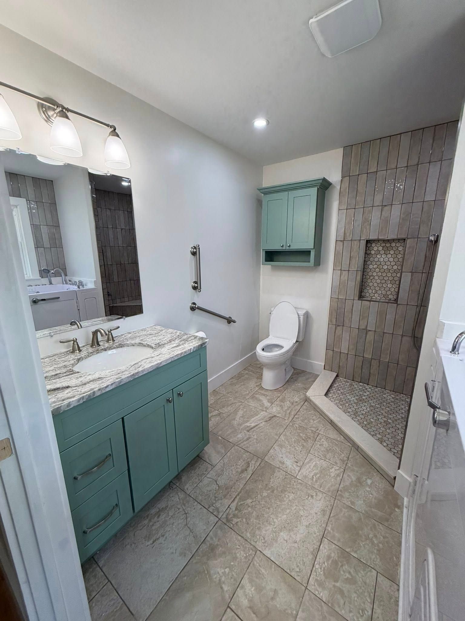 Modern bathroom with teal vanity, white toilet, mirror, and tiled shower.
