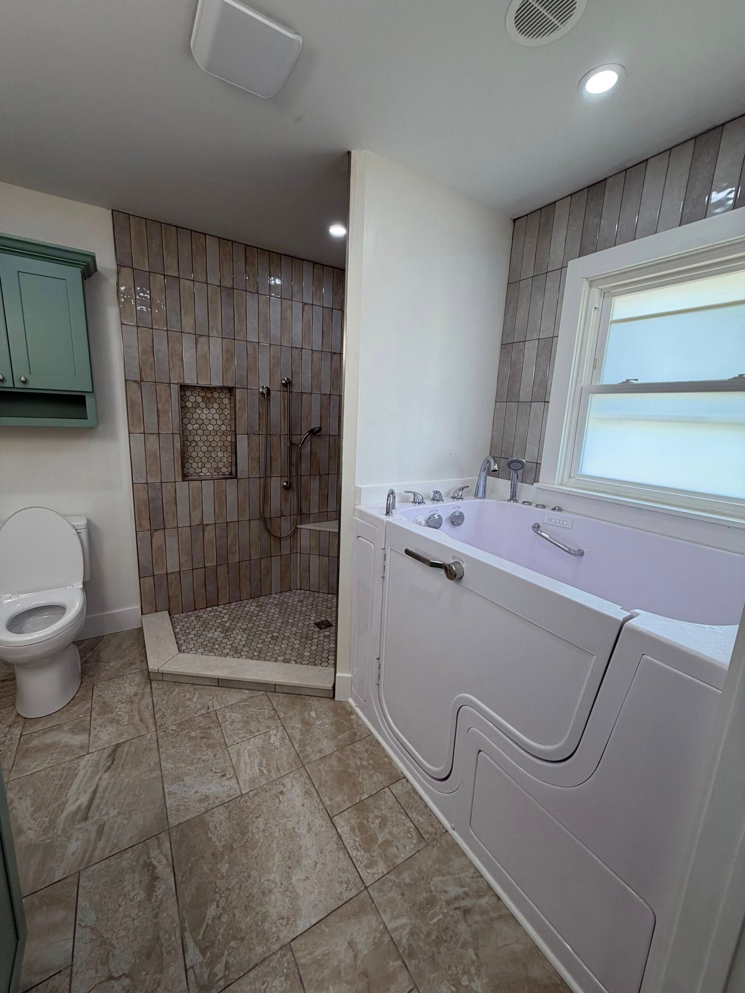 Bright bathroom with toilet, tiled shower, vanity, and window letting in daylight