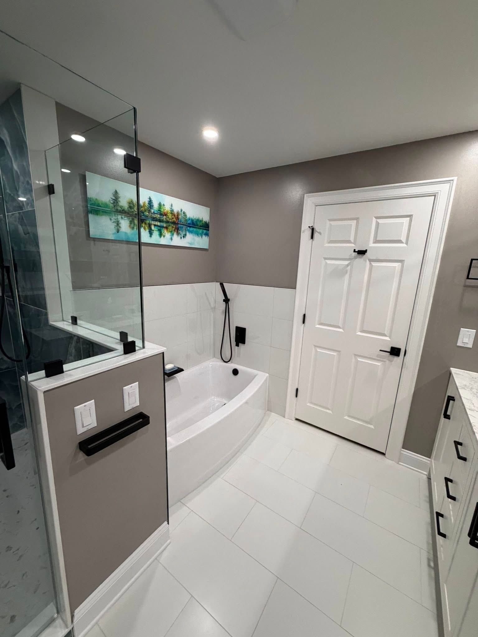 Modern bathroom with white tub, glass shower, vanity, and closed white door