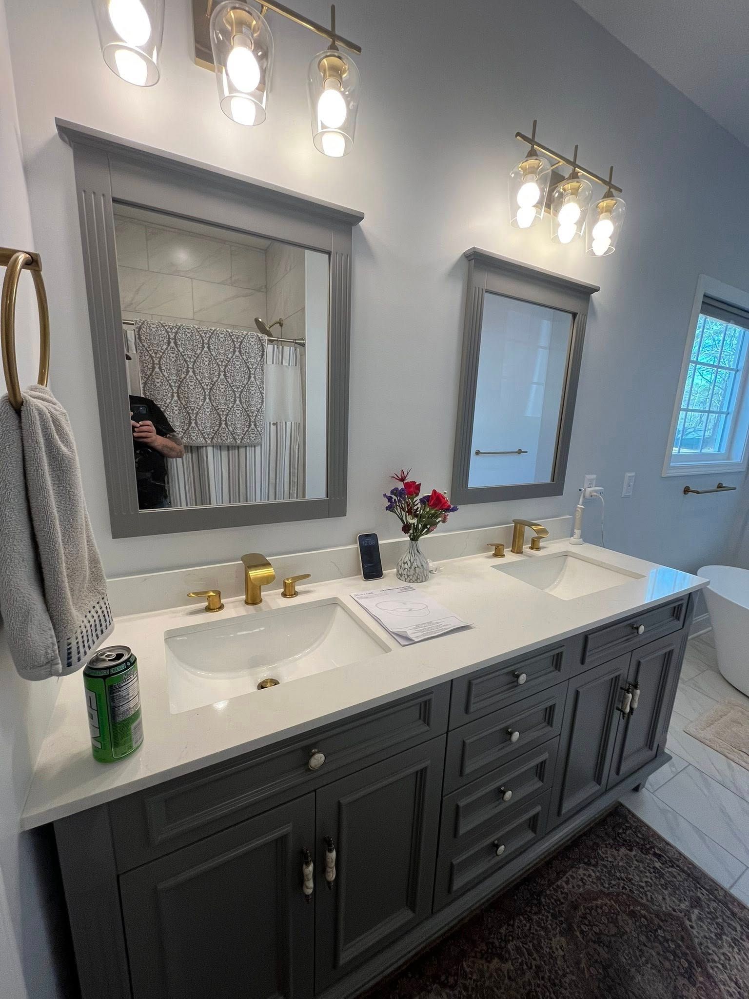 Modern bathroom vanity with double sinks, gray cabinets, gold fixtures, and two mirrors under wall lights