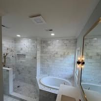 Modern white-tiled bathroom with walk-in shower, freestanding tub, and large mirror.