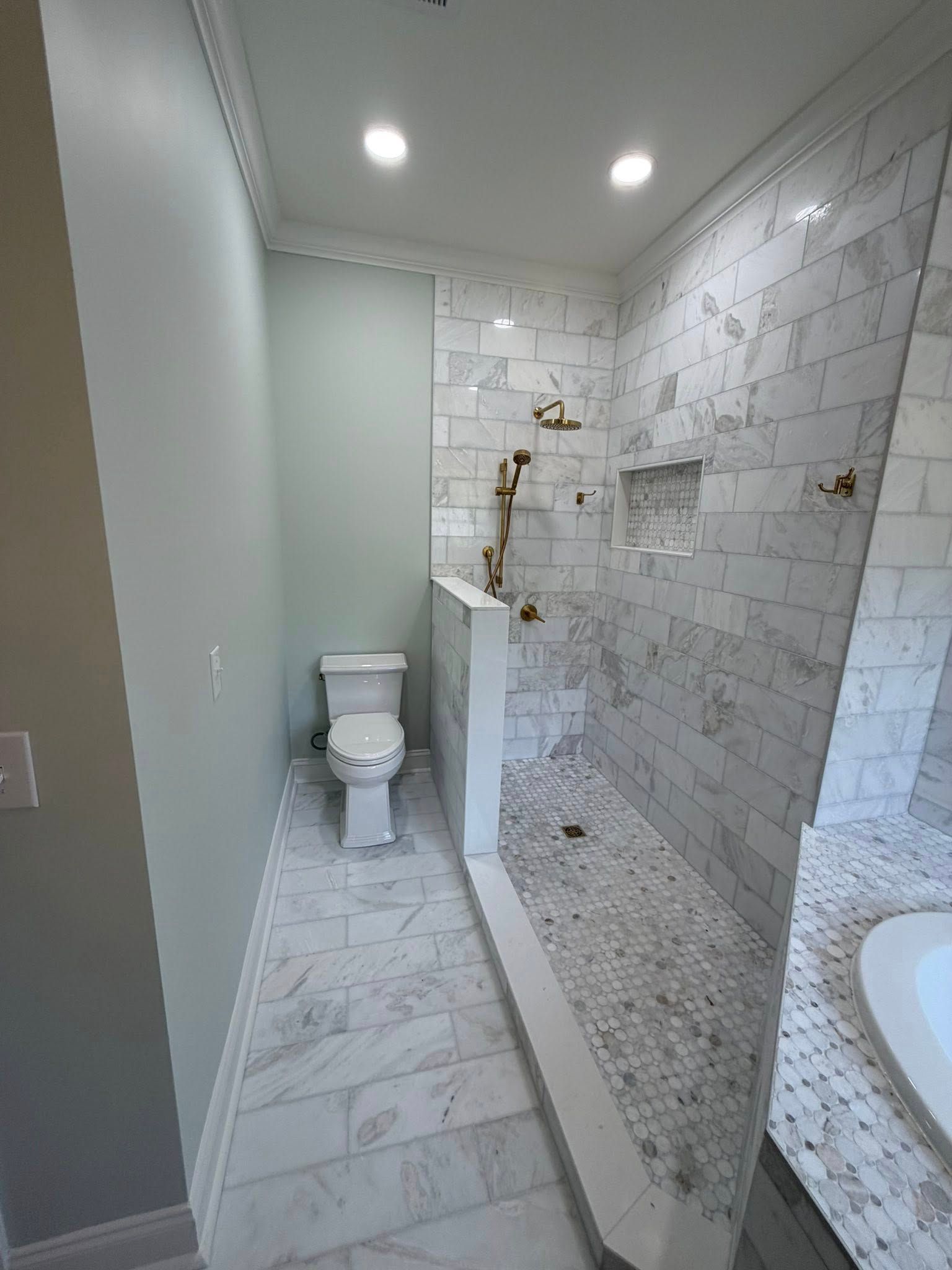 Narrow bathroom with marble tile, toilet, glass shower, and sink under recessed lights