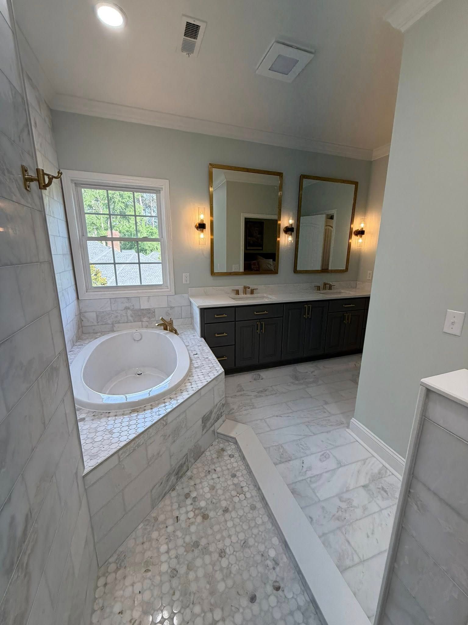 Elegant bathroom with white tiled jacuzzi tub, marble floor, dark vanity, and gold-framed mirrors.