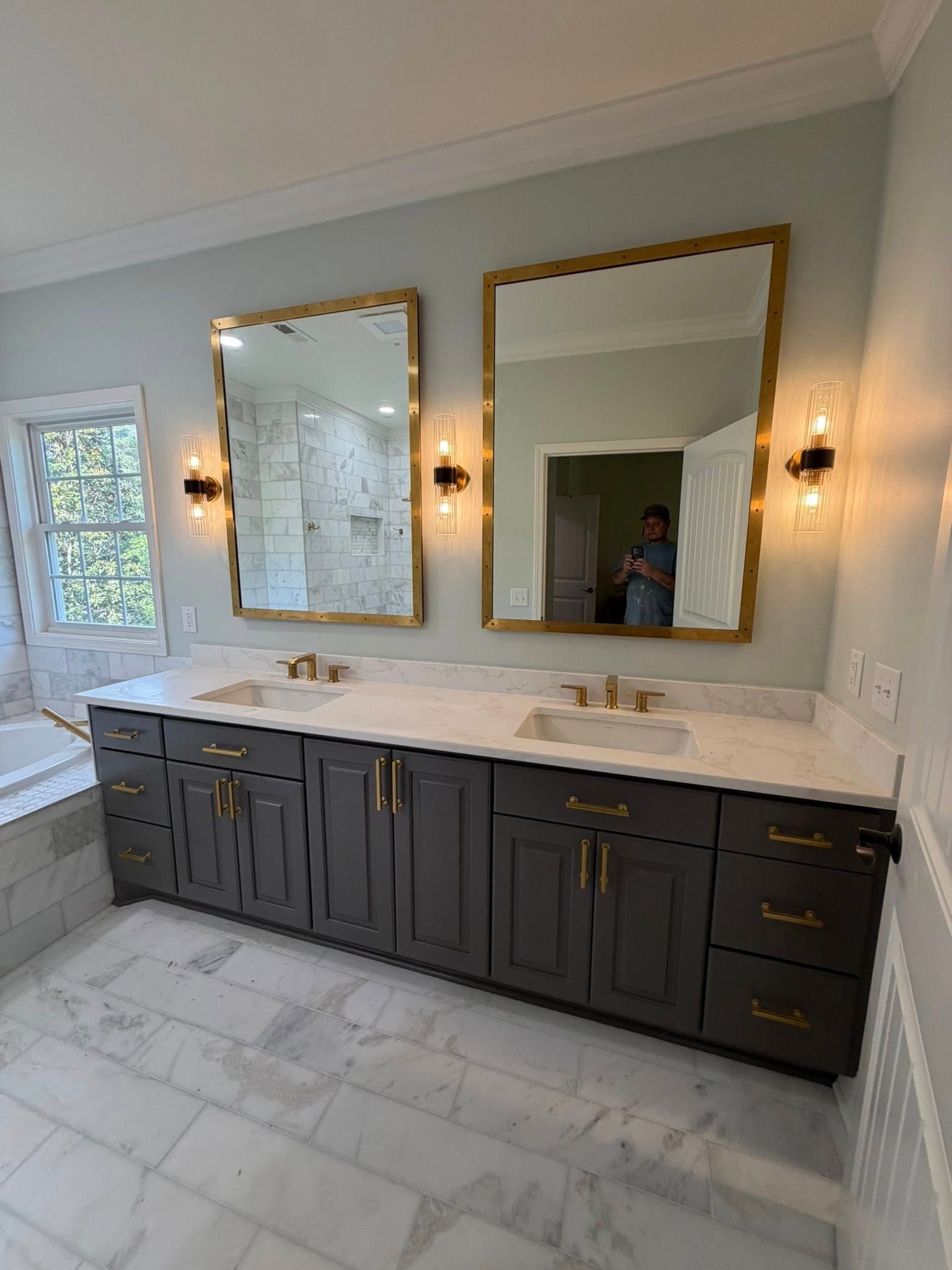 Modern bathroom vanity with dark cabinets, marble countertop, and large gold-framed mirrors under wall sconces
