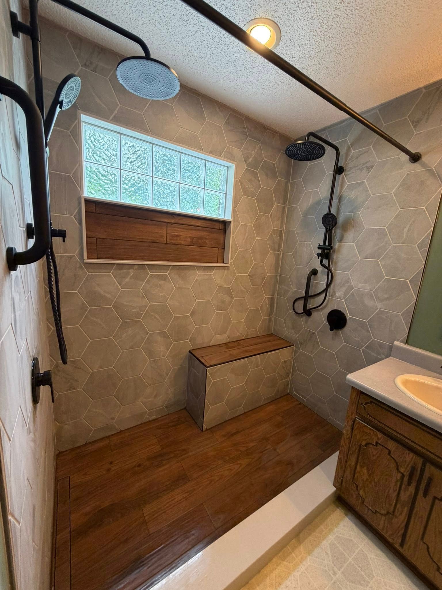 Walk-in shower with wood-look floor, patterned tile walls, window, bench, and black shower fixtures