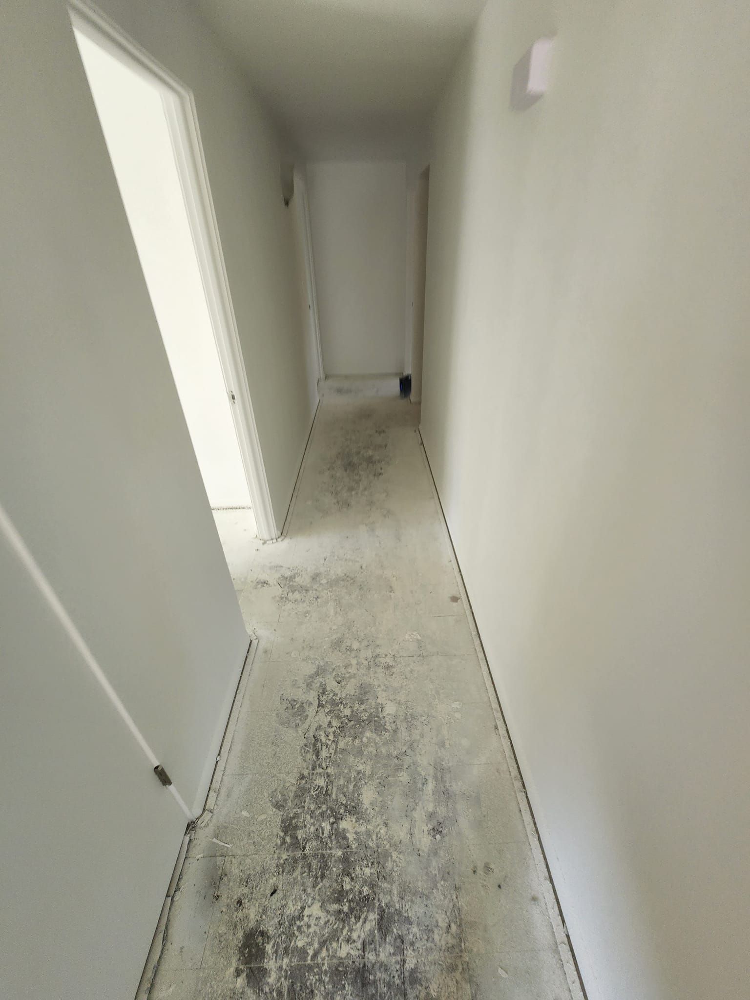 A long hallway with a dirty floor and white walls.