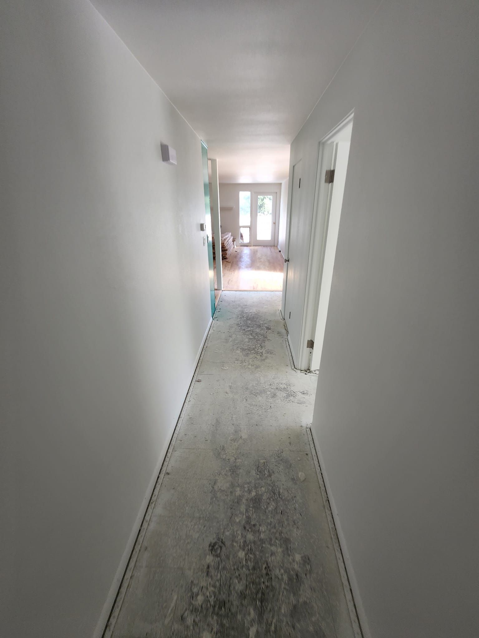 A long hallway with white walls and a carpeted floor leading to a living room.