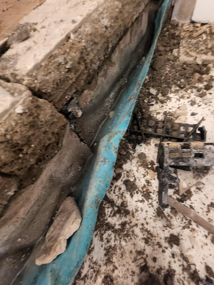 A close up of a drain on the ground next to a brick wall.
