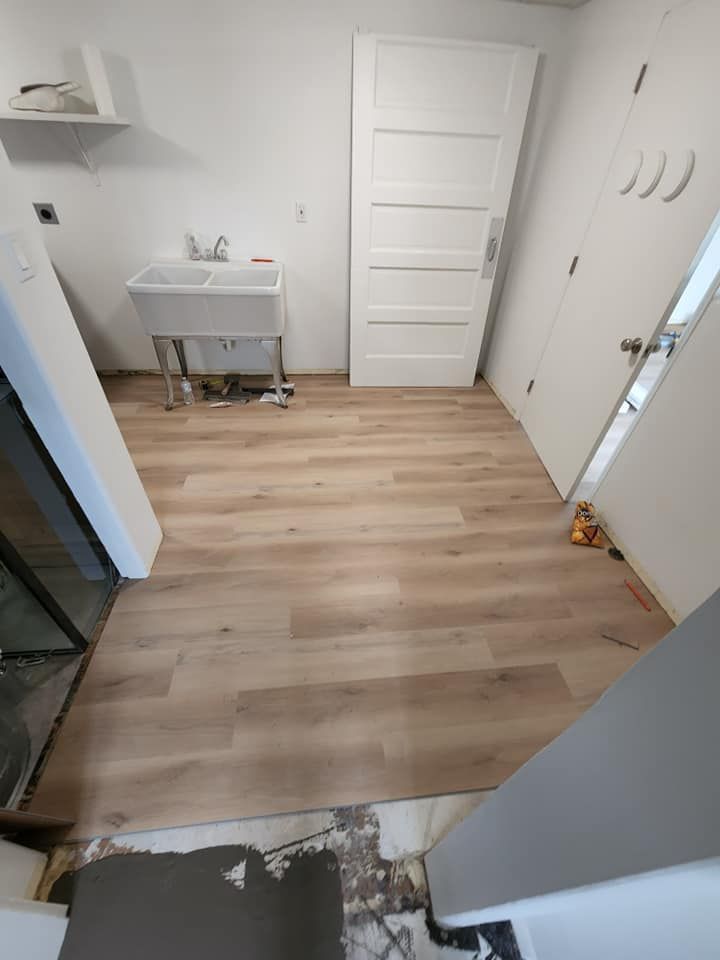 A laundry room with a sink and a wooden floor.