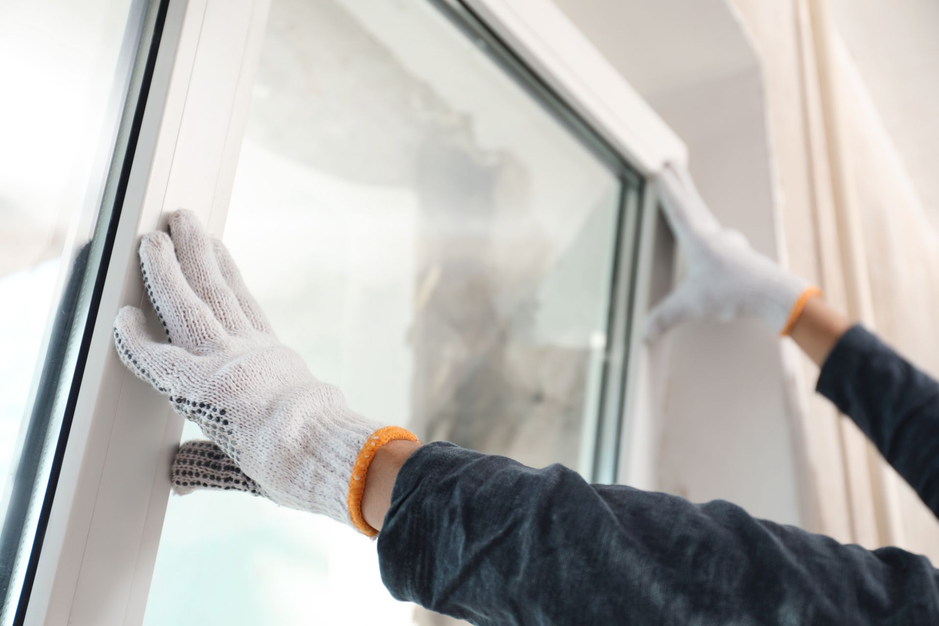 A person wearing gloves is cleaning a window with a cloth.