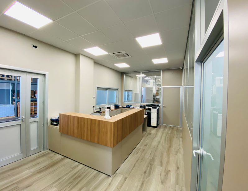 Area reception moderna con scrivania in legno, pareti in vetro e luci a soffitto brillanti.