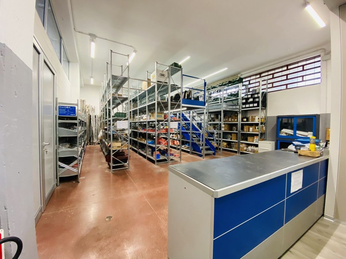 Allée lumineuse d'entrepôt avec comptoirs de rangement bleus, étagères métalliques et cartons sous éclairage fluorescent