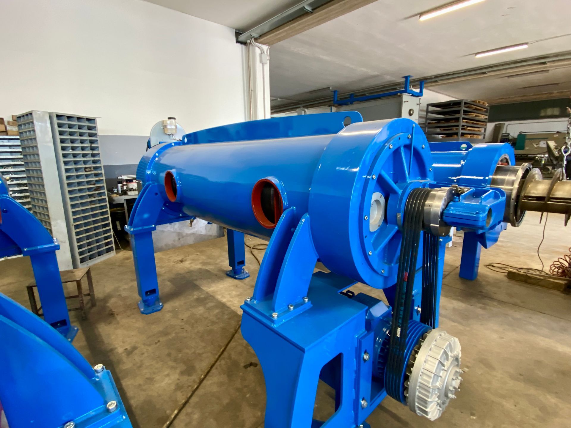 Macchinario industriale blu in un'officina, con grande involucro cilindrico e ingranaggi a vista.