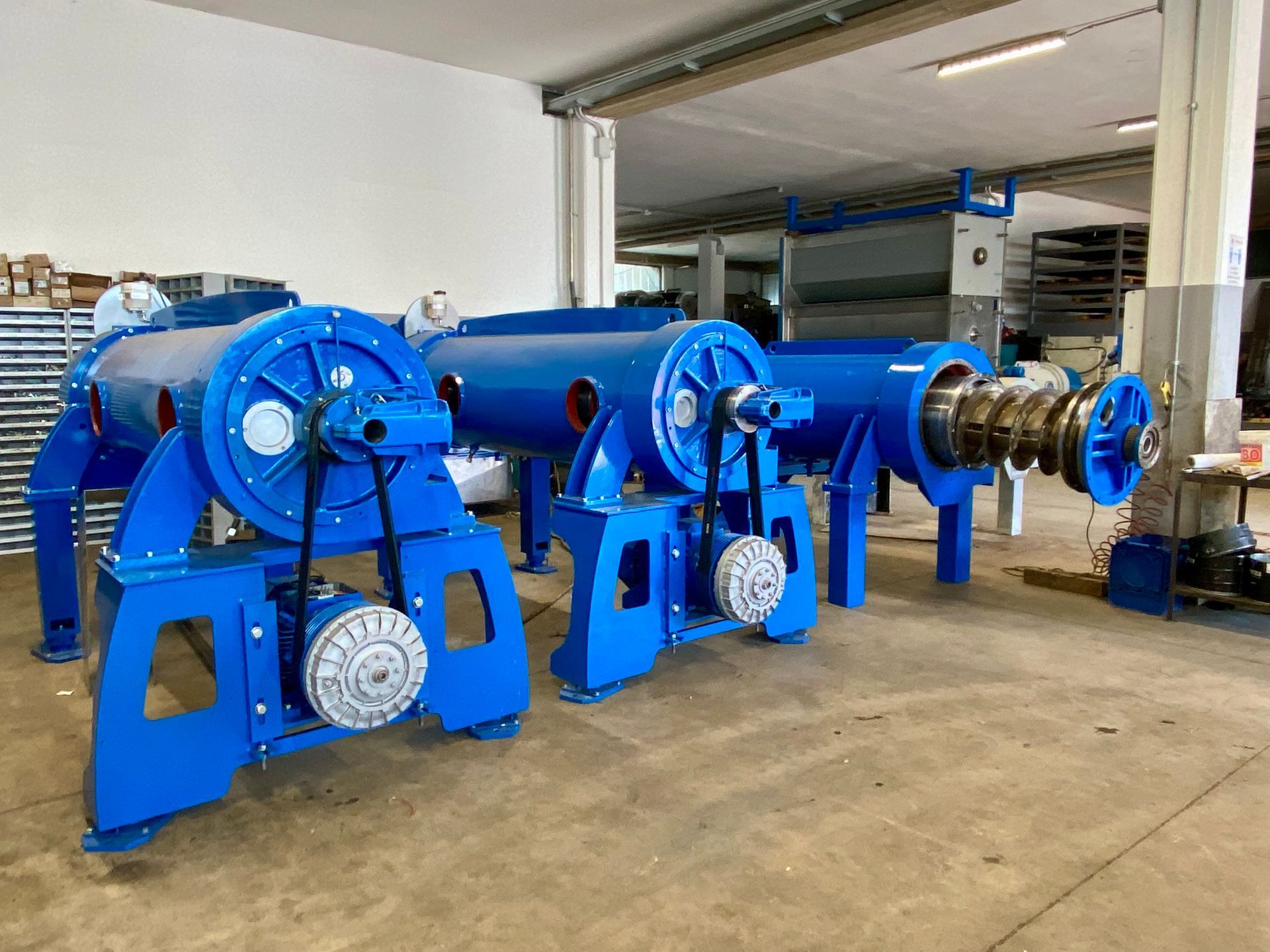 Macchinari industriali blu in un'officina, tra cui diversi grandi avvolgicavo e motori sul pavimento.