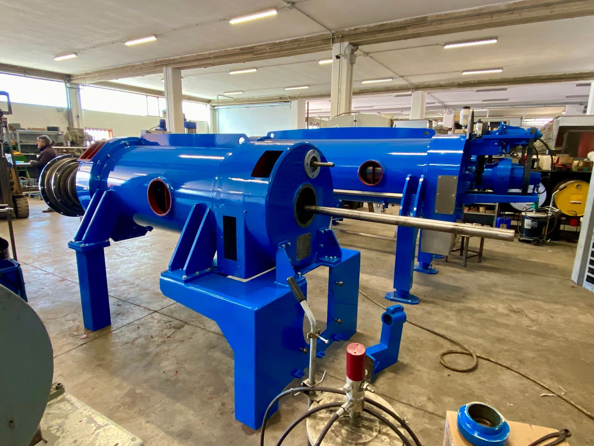 Macchinario industriale di colore blu brillante in un'officina, montato su supporti con tubi e utensili nelle vicinanze.