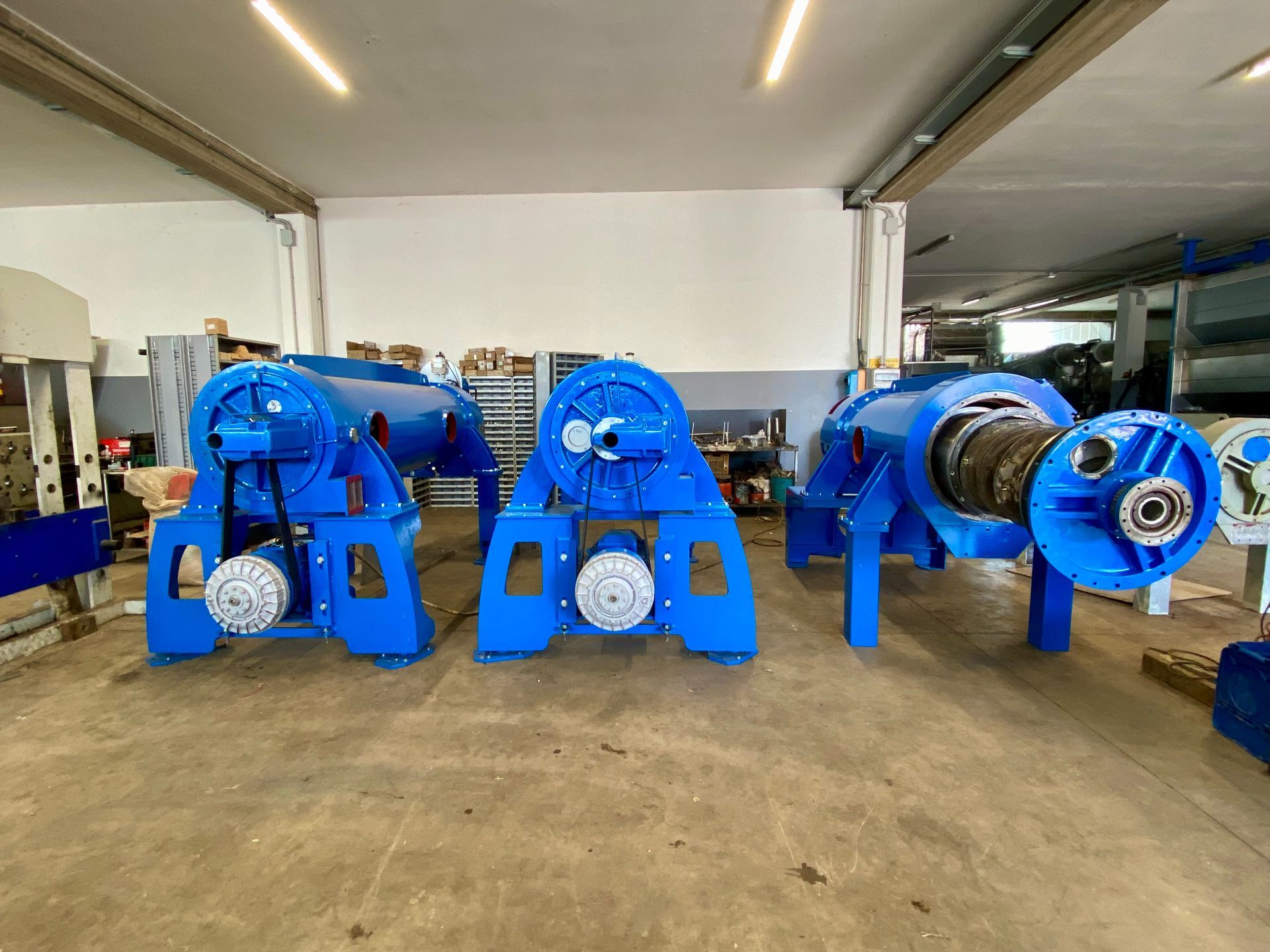 Tre macchine industriali blu in un'officina, allineate su un pavimento di cemento.