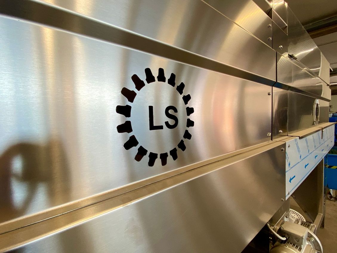 Machine en acier inoxydable brossé avec un logo « LS » et un emblème noir en forme d'engrenage sur le côté.