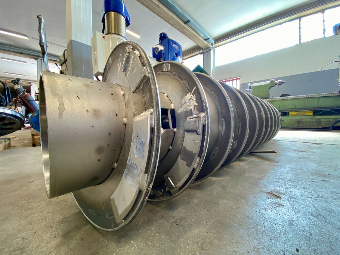 Un grand rotor de turbine industrielle en métal gisant sur le sol d'une usine sous une lumière vive.
