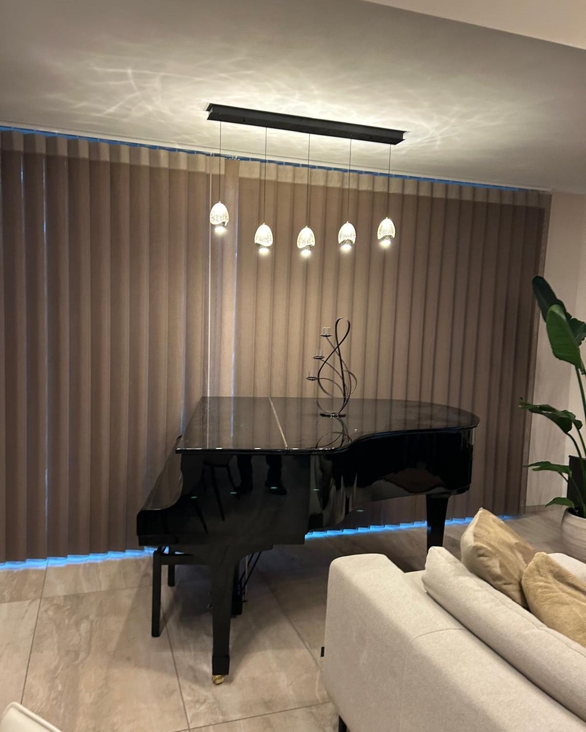 Pianoforte a coda nero in un soggiorno moderno con lampade a sospensione e divano beige.