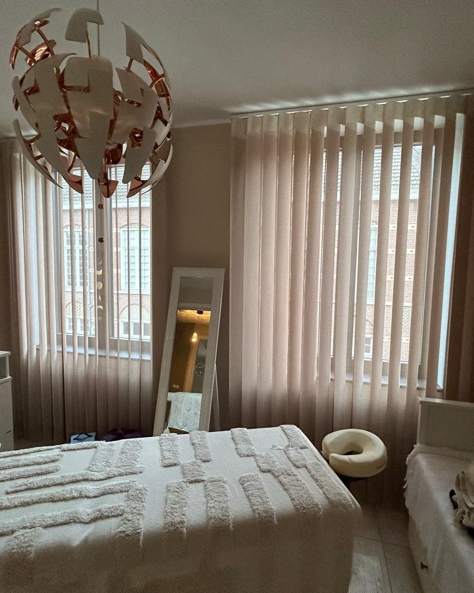 Accogliente camera da letto con letto, specchio a figura intera, tende color crema e un lampadario a sospensione vicino alla finestra.