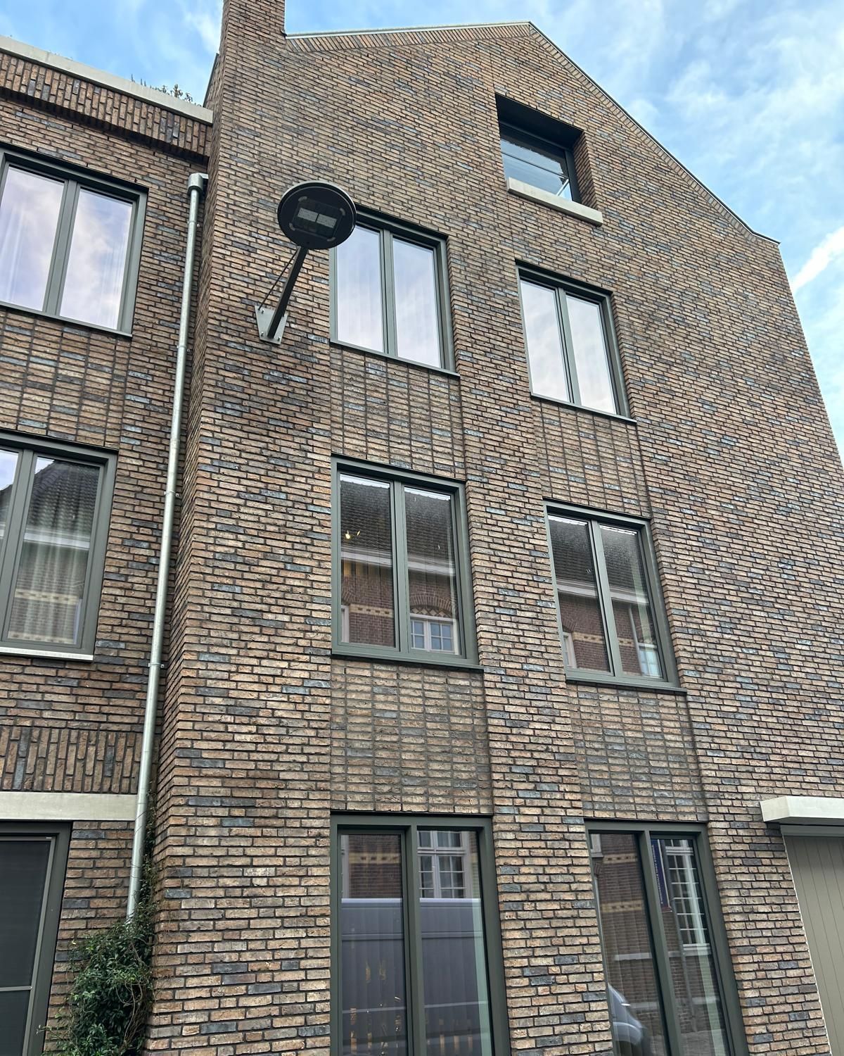 Facciata di un palazzo in mattoni con finestre e un'antenna parabolica nera sotto un cielo blu.