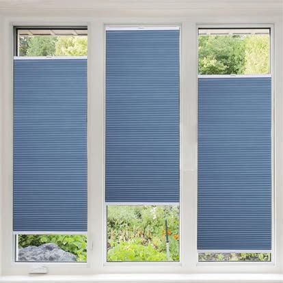 Tre finestre con tende a pieghe blu, la tenda centrale sollevata per mostrare il verde all'esterno.