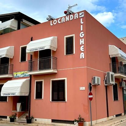 Edificio d'angolo rosa con tende da sole bianche e insegna con la scritta
