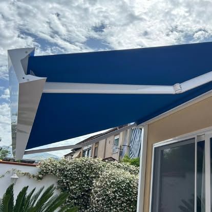 Tenda da sole blu retrattile sopra un patio accanto a una casa sotto un cielo nuvoloso