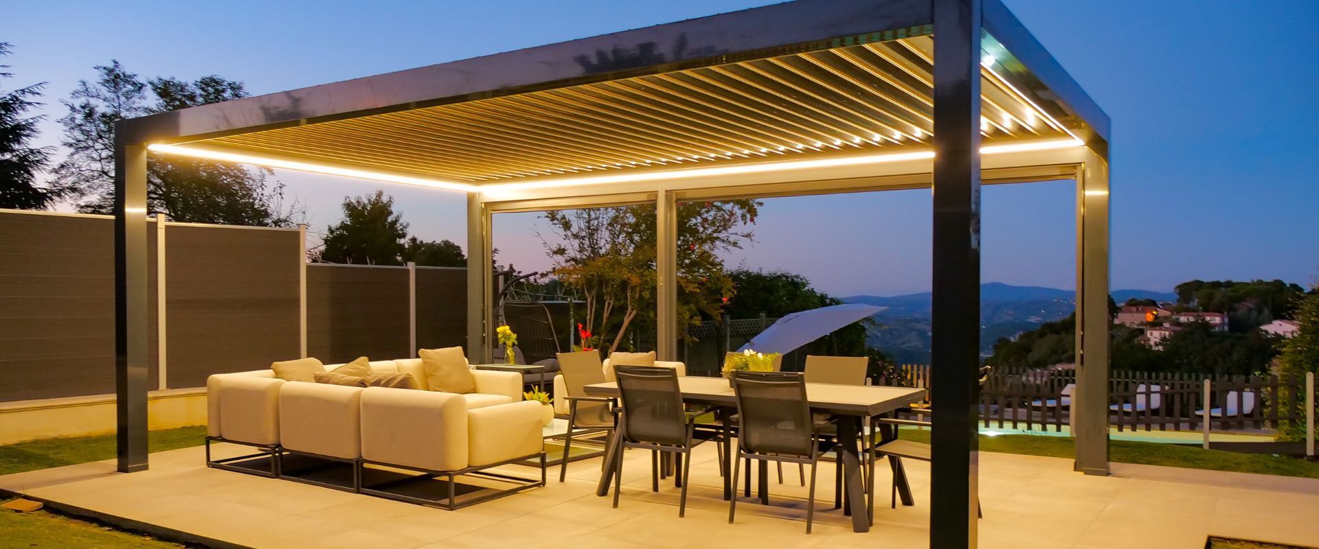 Patio esterno con pergola moderna, luci decorative, divani e tavolo da pranzo al tramonto