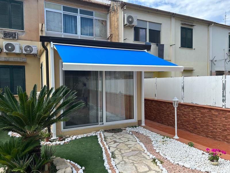 Piccolo patio con tenda da sole blu, porta scorrevole in vetro e sentiero in pietra paesaggistico.