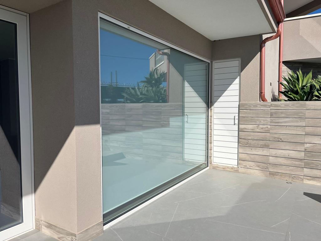 Patio moderno con porta scorrevole in vetro, pareti beige e un basso muretto in pietra per la privacy, esposto alla luce del sole.