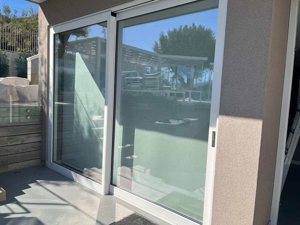 Porte scorrevoli in vetro su un patio, che riflettono la zona salotto esterna illuminata dalla luce del sole.