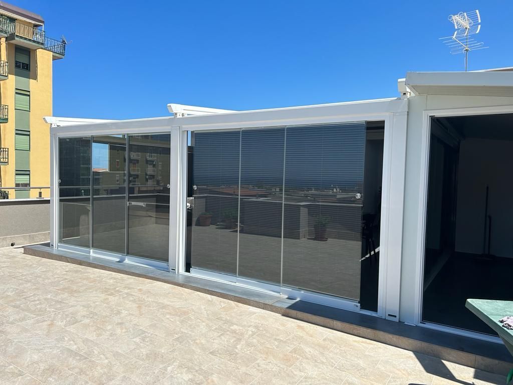Moderno patio esterno con pareti in vetro e un'apertura ombreggiata sotto un cielo azzurro limpido.