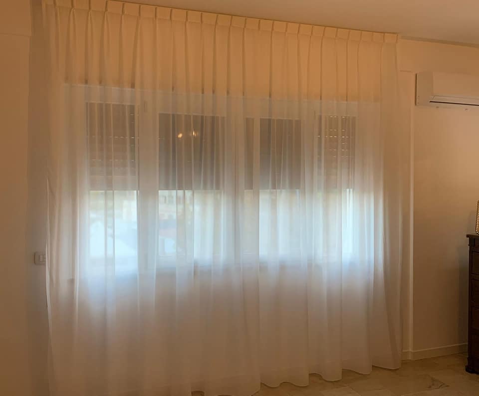 Tende bianche trasparenti che coprono una finestra luminosa in una stanza beige